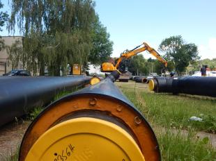Csővezetékek hevernek az Ózdi Szakképzési Centrum Gábor Áron Technikum és Szakképző Iskola udvarán, a távolban egy markológép látható.
