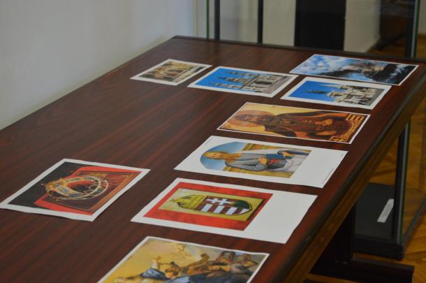 Címerek, templomok és szentek fotói láthatóak az asztalon.