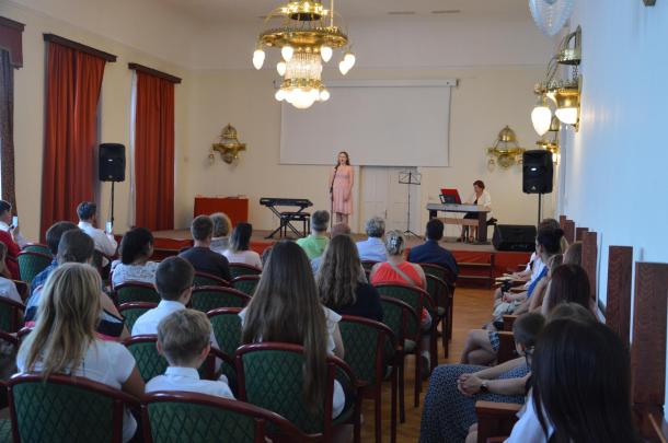 Az Olvasó Adorján Lajos termében a zeneiskola diákjai foglalnak helyet, valamint egy tanítvány és egy pedagógus a színpadon szerepel.