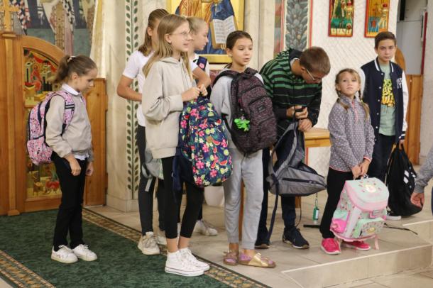Gyerekek állnak iskolatáskával a kezükben és várják az áldást.