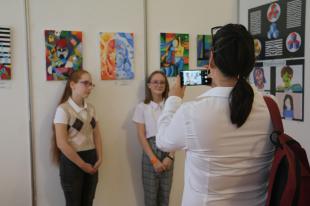 A pedagógus fotózza a fiatalokat a festmények előtt.