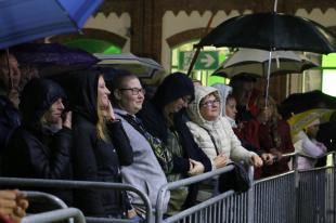 Esernyővel állnak a koncert résztvevői a kordonnál.
