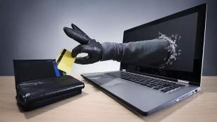 Laptopon keresztül kinyúló kéz, ami elveszi a pénztárcából a bankkártyát.