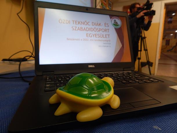 Az Ózdi Teknőc Diák- és Szabadidősport Egyesület kabalafigurája, egy kis játék teknős figyel a laptopon.