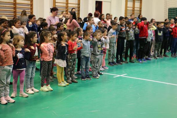 Gyerekek énekelnek és táncolnak az intézmény tornatermében.
