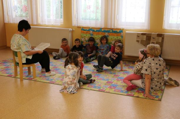 A kisgyermeknevelők és az apróságok a szőnyegen ülve tanulják az énekeket.
