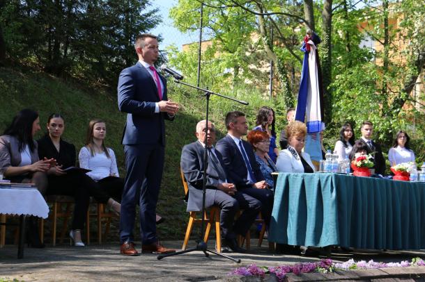 Janiczak Dávid, Ózd város polgármestere beszédet mond az ünnepségen. A mellette lévő asztalnál a meghívott vendégek ülnek.