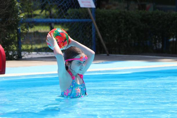 A kislány eldobja a labdát a medencében.