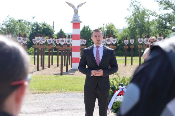 Janiczak Dávid polgármester a megjelentekhez szól, mögötte pedig a Trianoni emlékpark látható.