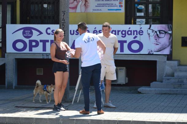 Janiczak Dávid, polgármester átadja a vizet egy kutyát sétáltató járókelőknek.
