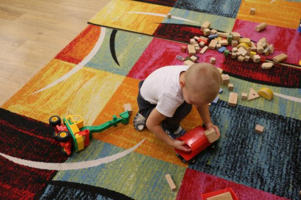 A kisfiú a szőnyegen fakockákkal játszik.