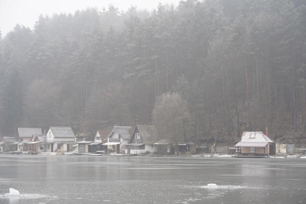 Távoli kép a befagyott tóról és a túlparton álló házakról.