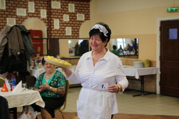 Az egyik hölgy pincérnő jelmezben szolgálja fel a süteményt.