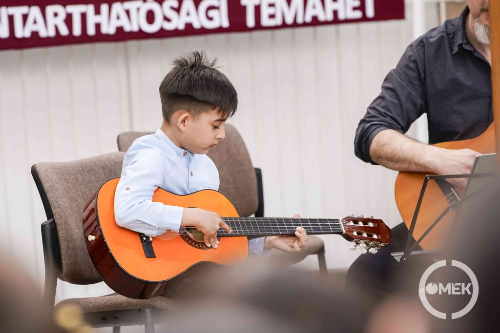 Egy kisfiú gitározik.