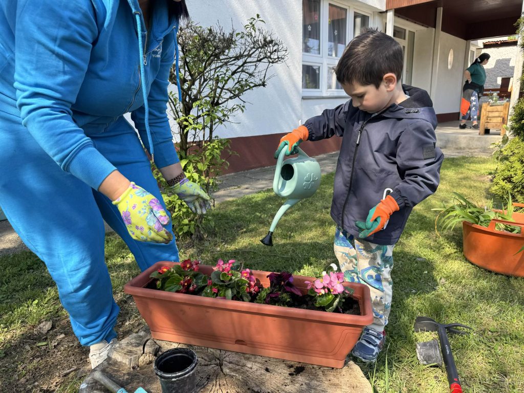 Egy kisfiú locsolja a virágokat.