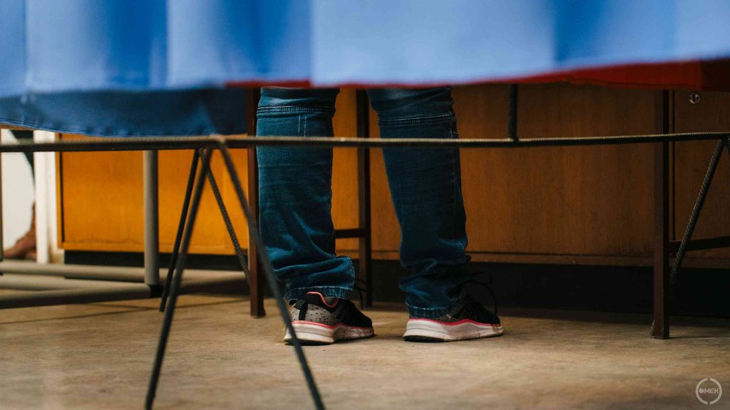 Lábak látszanak a szavazófülke függönye alatt.