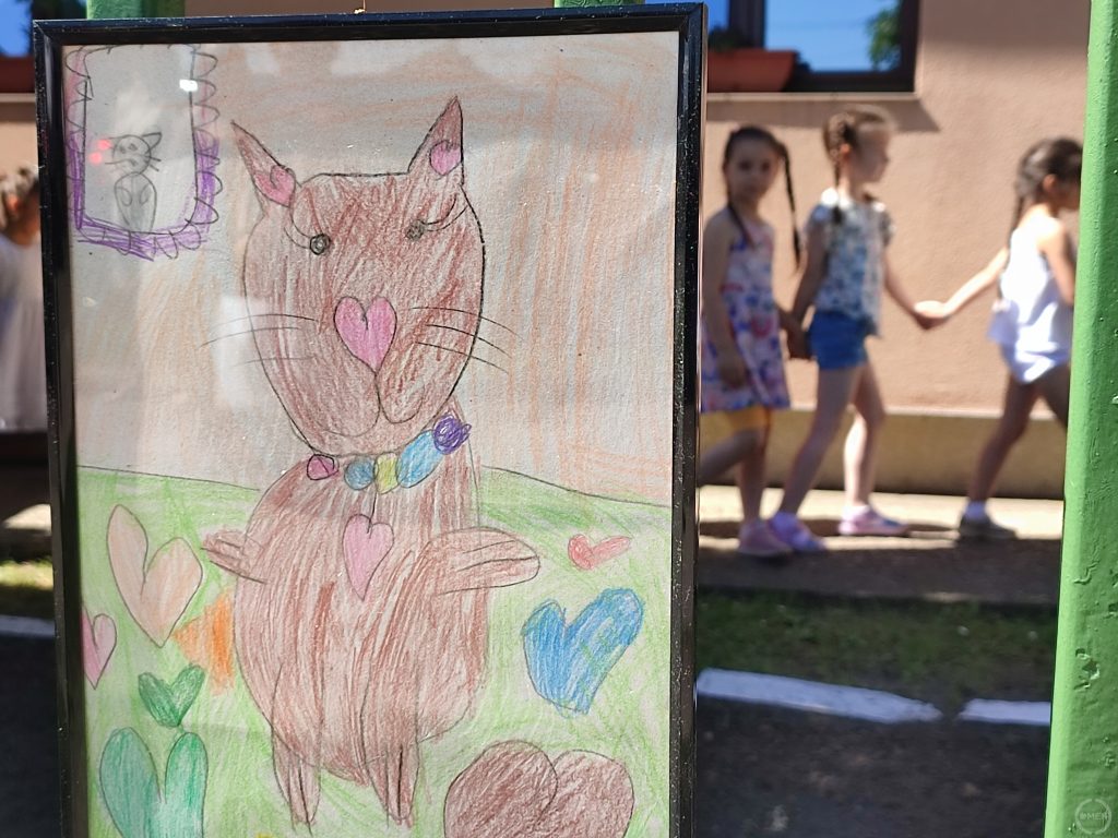 Egy cica a képen, gyerekek a háttérben.