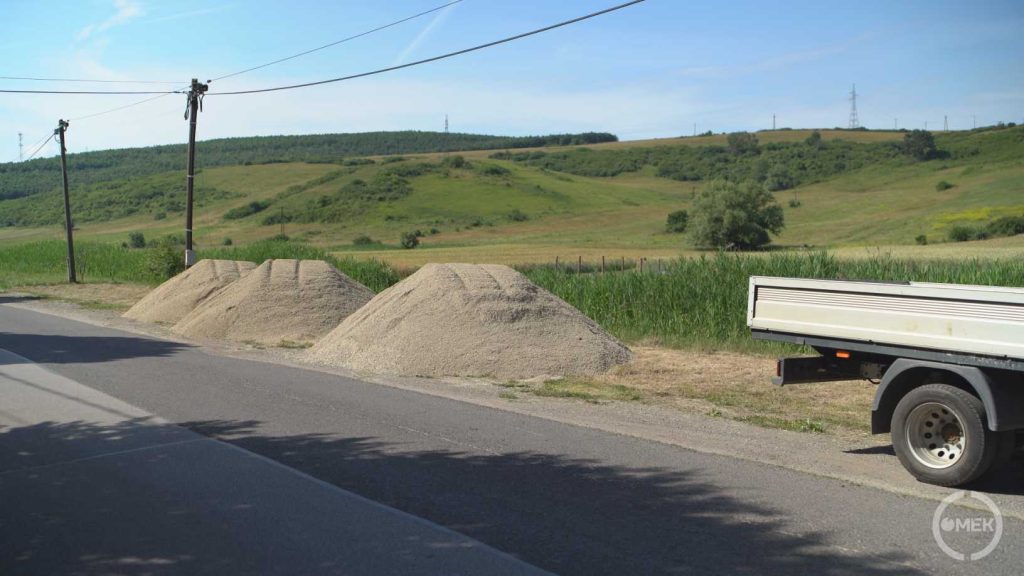 Homokos kavics és salak halmok várakoznak az út szélén.