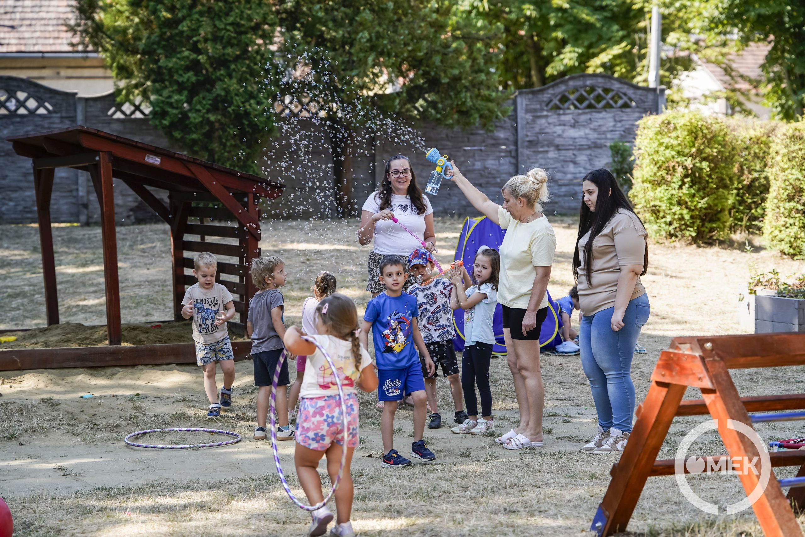 Az óvónők buborékfújóval szórakoztatják a gyerekeket.
