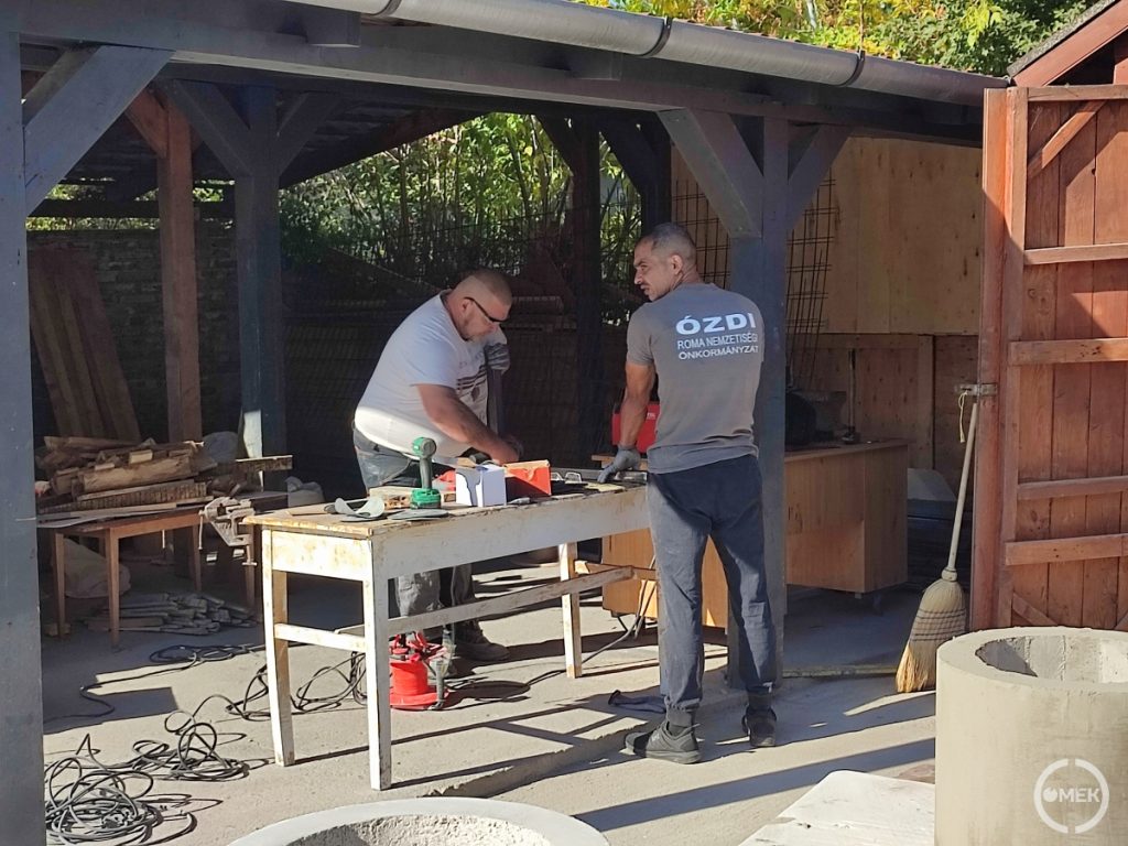Két dolgozó munkálkodik az asztalnál.